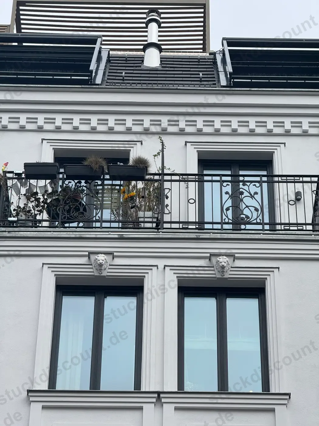 Fassadendetail mit Balkon, Zierband und dekorativen Löwenköpfen